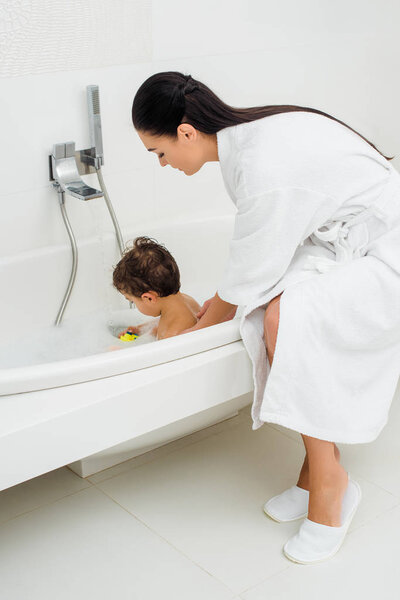 Mother in bathrobe washing son in bathroom 