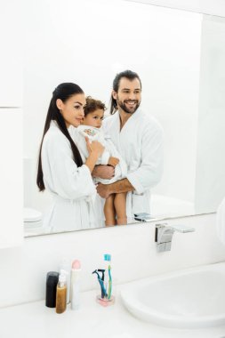 Family looking in mirror and smiling in white bathroom  clipart