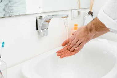 Beyaz banyo içinde akan suyun altında erkek eller 