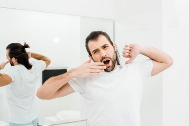 Man in T-shirt stretching and yawning in white bathroom clipart