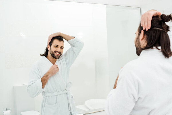 Handsome man looking in mirror and smiling in white bathroom 
