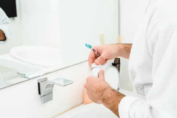 在浴室里拿着牙膏和牙刷的男性手的裁剪视图 — 图库照片
