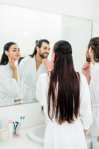 young couple in white bathrobes looking at mirror in bathroom