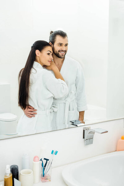 tender couple  in white bathrobes hugging in bathroom at morning 