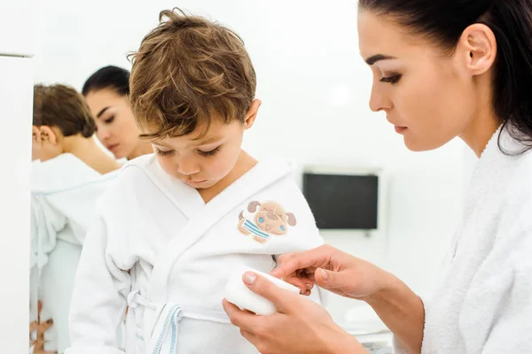 Madre Che Tiene Crema Idratante Viso Mentre Figlio Guarda Basso — Foto Stock