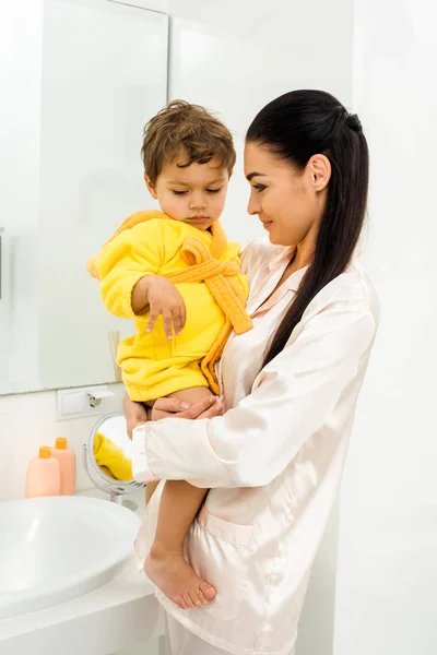 Sonriente Feliz Madre Sosteniendo Hijo Amarillo Albornoz —  Fotos de Stock