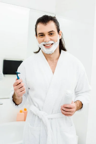 Man with shaving accessories smiling in bathroom