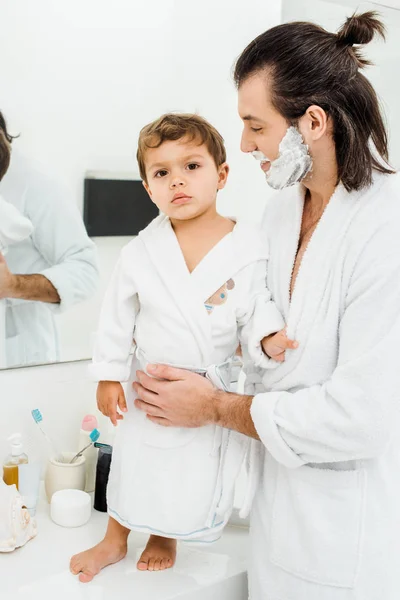 Hombre Guapo Albornoz Sonriendo Mirando Hijo Pequeño — Foto de stock gratuita