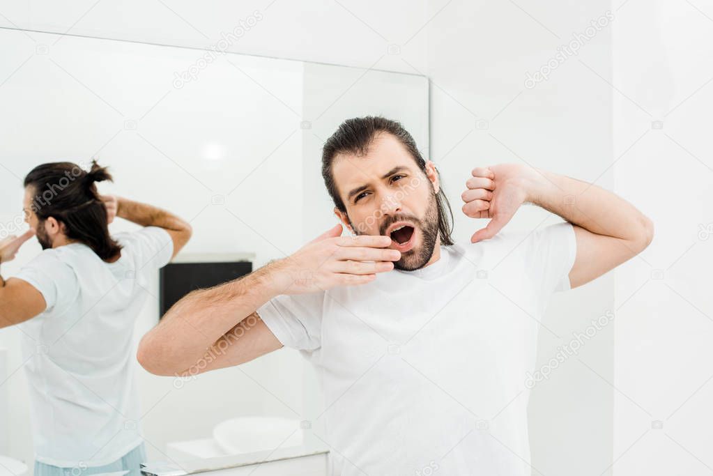 Man in T-shirt stretching and yawning in white bathroom