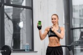 attractive athletic sportswoman pointing on smartphone with medical appliance in gym