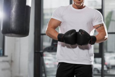 Kas boksör boks eldivenleri yakınındaki kum torbası içinde jimnastik salonu ile ayakta kırpılmış görüntü