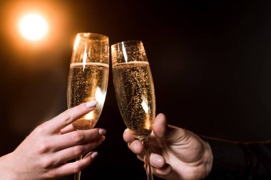 cropped shot of couple clinking glasses of champagne under golden light on black clipart