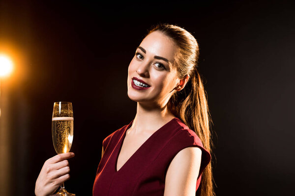 smiling young woman holding glass of champagne on black