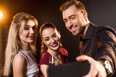 group of happy people taking selfie with smartphone during party on black clipart