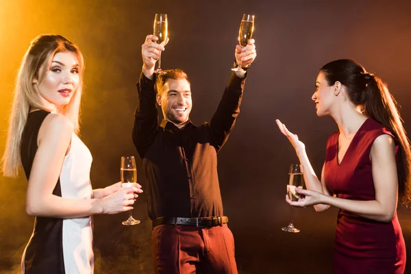 group of happy people toasting with champagne glasses under golden light on black