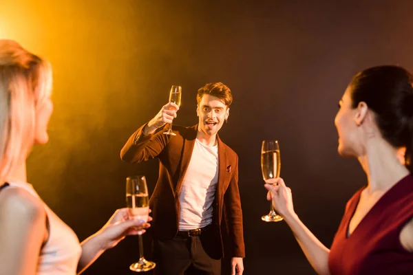 group of people toasting with champagne glasses under golden light on black