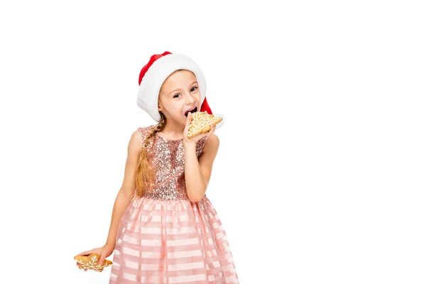 サンタ帽子食べる生姜クッキーおよび白で隔離カメラ目線の幸せな小さな子  — 無料ストックフォト