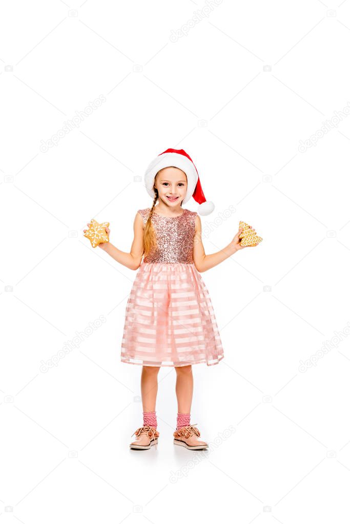 smiling little child in santa hat with ginger cookies looking at camera isolated on white