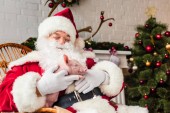 glücklicher Weihnachtsmann hält Schwein und sitzt im Schaukelstuhl