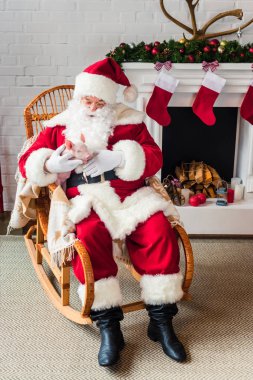 high angle view of santa claus holding pig and sitting in rocking chair clipart