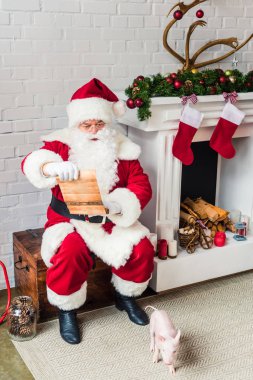 high angle view of santa claus sitting on chest near fireplace and reading wish list clipart