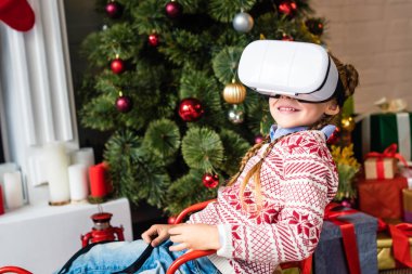 kızak içinde oturan ve sanal gerçeklik kulaklık Noel zamanı kullanarak sevimli gülümseyen çocuk