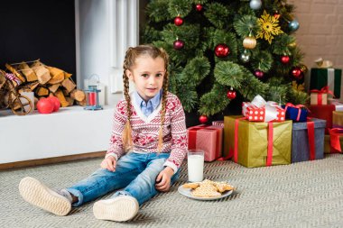 gingerbread çerezleri ve Noel ağacının yanında oturan ve kameraya bakarak süt ile sevimli çocuk