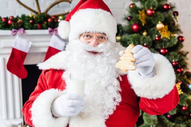 happy santa claus holding gingerbread cookie and glass of milk clipart