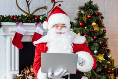 Noel dizüstü kullanarak ve şömine yakın kamera bakıyor 