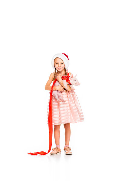 adorable little child in santa hat holding piggy and looking at camera isolated on white