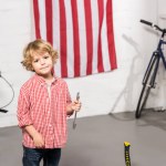 Селективный фокус маленького ребенка, стоящего с гаечным ключом рядом с велосипедами в мастерской Селективный фокус маленького ребенка, стоящего с гаечным ключом рядом с велосипедами в мастерской