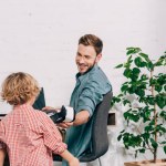 Laughing man giving virtual reality headset to little son