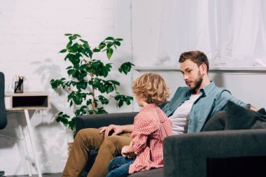 seçici odak konuşuyor ve sevimli küçük oğluyla evde oturma odasında kanepede oturan adamın