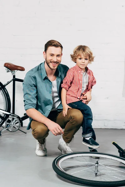 幸せな男の小さな息子と座っていると自転車ワーク ショップでカメラ目線  — 無料ストックフォト