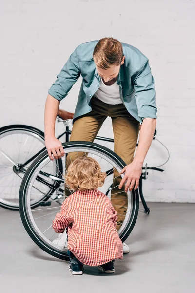 少年の父親のワーク ショップで支援しながら自転車の車輪を修理の背面図  — 無料ストックフォト