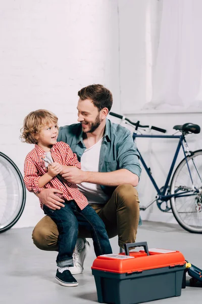 Lächelnder Mann Sitzt Mit Kleinem Sohn Neben Werkzeugkiste Fahrradwerkstatt — Stockfoto