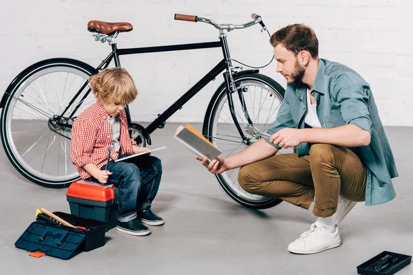 Kind Sitzt Mit Digitalem Tablet Während Vater Buch Fahrradwerkstatt Liest — Stockfoto