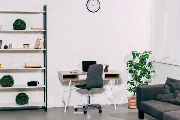 interior of modern living room with table, laptop, houseplant, shelves and sofa 
