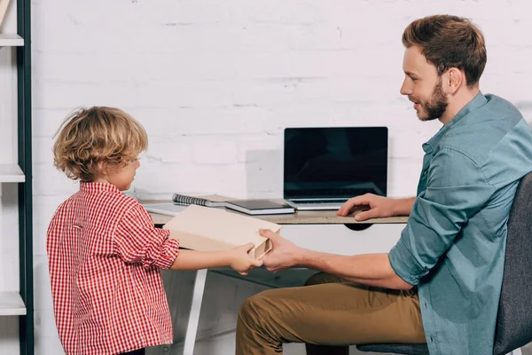 Homme Heureux Donnant Livre Petit Fils Près Table Avec Ordinateur — Photo gratuite