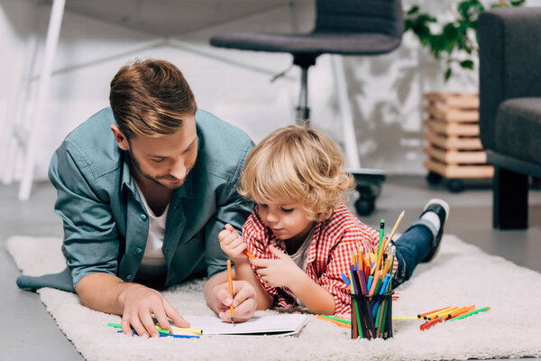 selective focus of father and son drawing on white paper by colorful markers at home