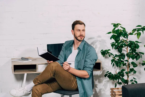 Freelancer Masculino Pensativo Sentado Com Livro Didático Olhando Para Mesa — Fotos gratuitas
