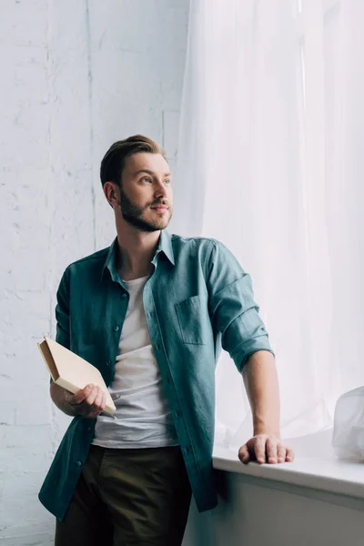 Low Angle View Young Man Book Looking Away Windowsill Home — Stock Photo, Image