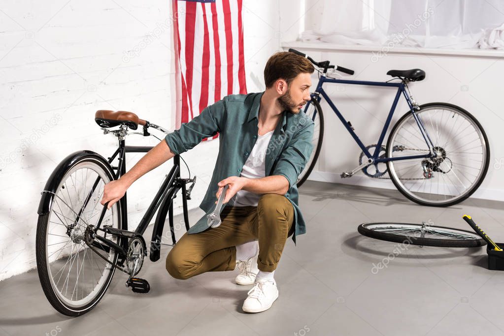 selective focus of young repairman fixing bicycle by adjustable wrench