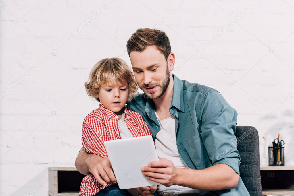 happy man showing digital tablet to little son at home