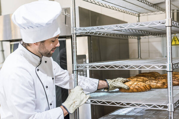 adult male baker touching fresh baked bread on kitchen rack