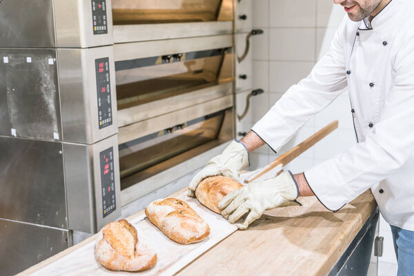 baker standing near oven with hot baked bread on wooden counter