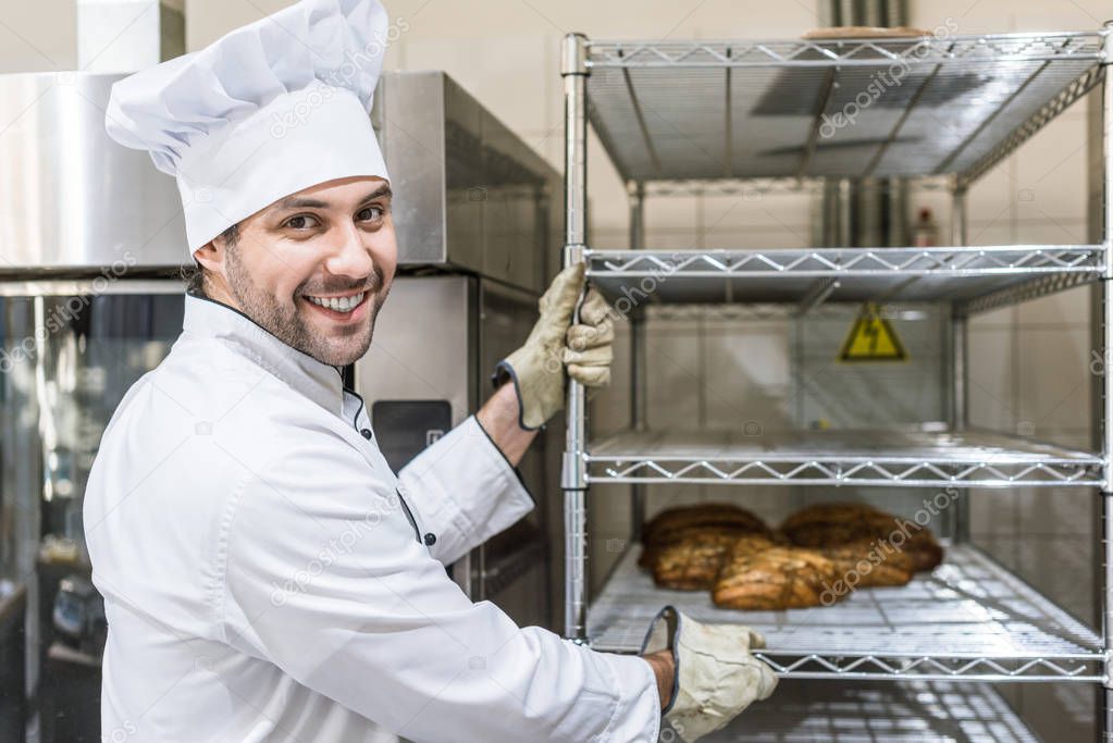 smiling male baker with hot baked bread on rack