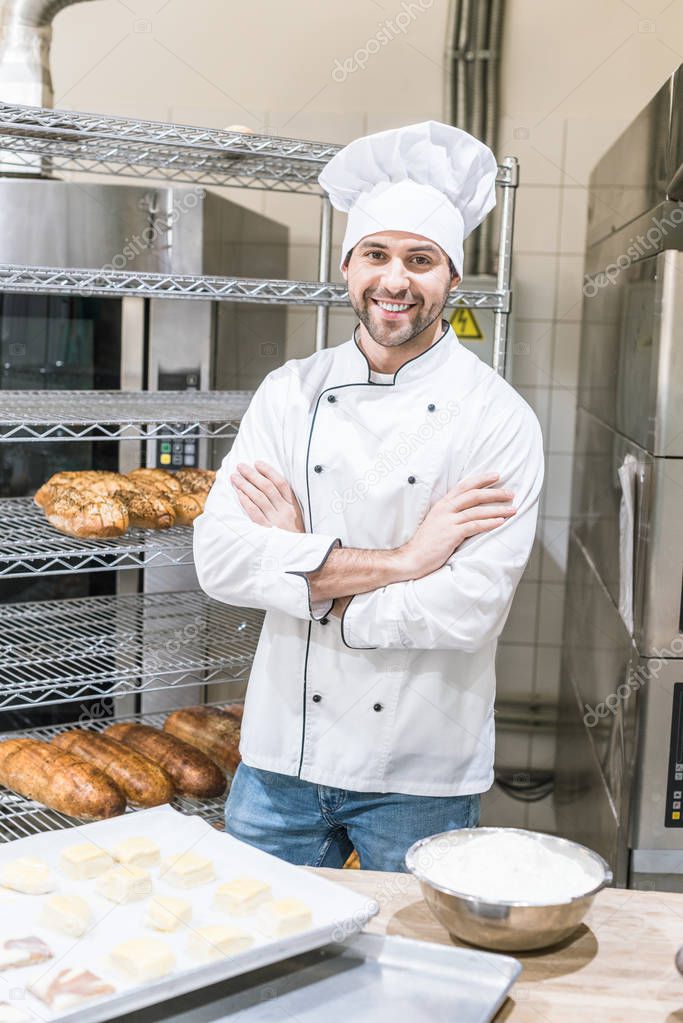 smiling male baker standing with arms crossed at kitchen