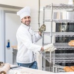 Panadero masculino sonriente en uniforme de chefs de pie en la cocina