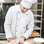 Cook in white chefs uniform kneading dough on wooden table